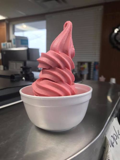 A swirl of pink soft serve ice cream in a white cup, sitting on a counter.