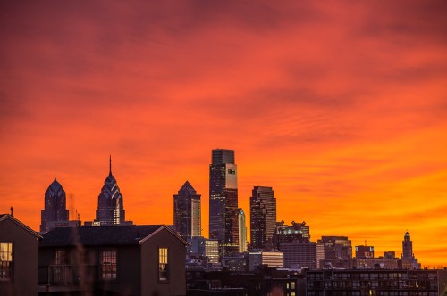Philadelphia skyline at sunset, with vibrant orange and purple hues illuminating the buildings.