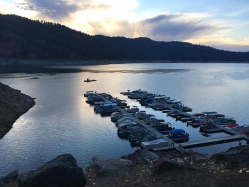 A serene lake at sunset with boats docked at a marina, surrounded by hills and a colorful sky.