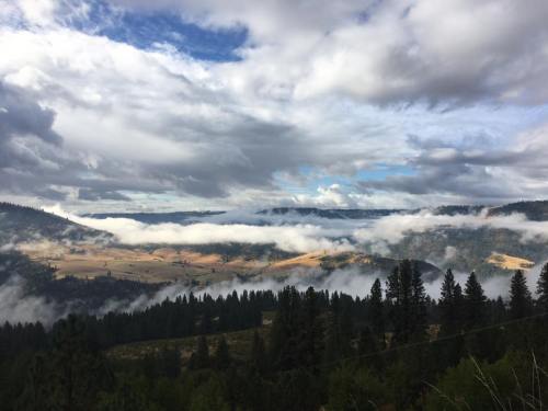 A scenic landscape featuring rolling hills, dense forests, and clouds hovering over valleys under a partly cloudy sky.