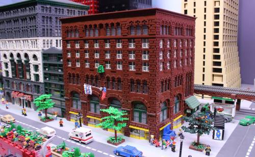 A detailed LEGO model of a historic brick building with flags, surrounded by miniature cars and trees.