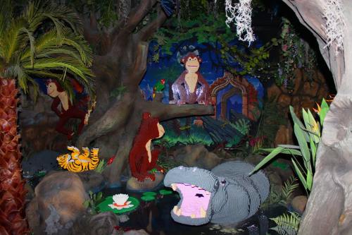 A vibrant jungle scene made of LEGO, featuring animals like monkeys, a tiger, and a hippo among lush greenery.