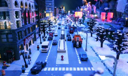 A vibrant LEGO city scene with cars, trees, and buildings, set in a snowy landscape with colorful lights.