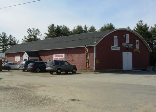 A red barn-style building with a large entrance, surrounded by parked cars and trees in the background.