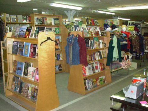 A cozy bookstore interior with wooden shelves filled with books and clothing displays in a well-lit space.