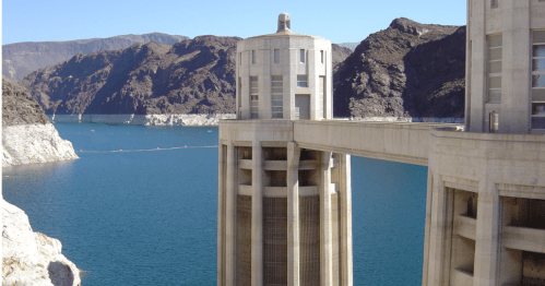 A concrete structure near a blue lake, surrounded by rocky mountains under a clear sky.
