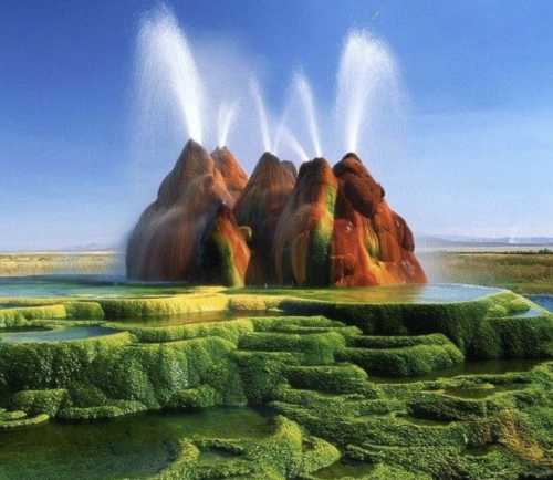 Colorful geothermal springs erupting from rocky formations, surrounded by vibrant green moss and a clear blue sky.