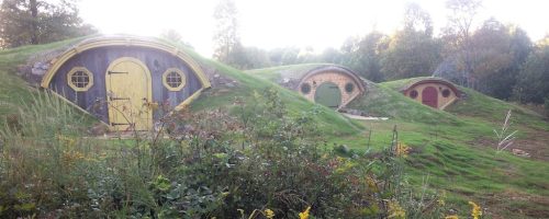 Three whimsical, rounded hobbit-style homes with colorful doors nestled in a grassy landscape.