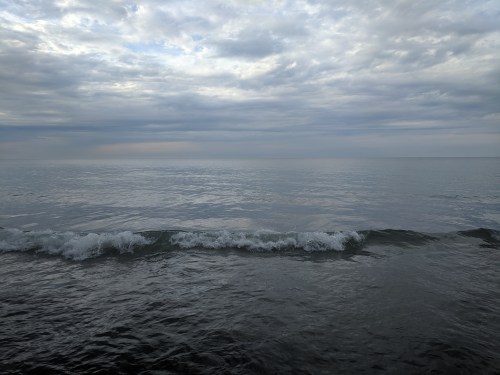 A calm ocean scene with gentle waves under a cloudy sky, reflecting soft light on the water's surface.
