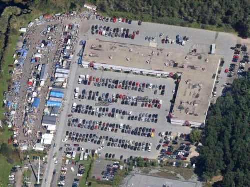 Aerial view of a busy outdoor market with numerous tents and a large parking lot filled with cars.