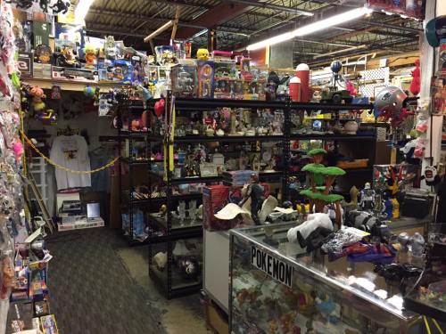 A cluttered store aisle filled with shelves of toys, collectibles, and various merchandise, including Pokémon items.