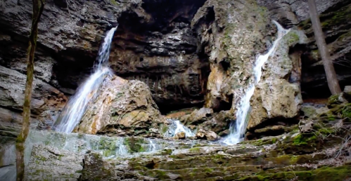 A serene waterfall cascading down rocky cliffs, surrounded by lush greenery and moss-covered stones.