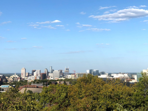 A panoramic view of a city skyline with modern buildings under a clear blue sky and scattered clouds.