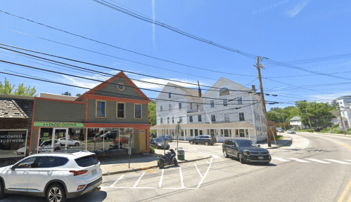 A street view featuring colorful buildings, power lines, and parked vehicles on a sunny day.