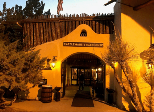Entrance of Cattleman's Steakhouse, featuring rustic architecture and warm lighting, with a person entering.