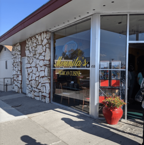 Exterior of Morenita's Mexican Cuisine, featuring a stone wall and large glass windows with an "Open" sign.
