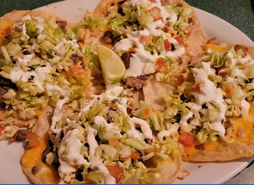 A plate of tacos topped with lettuce, tomatoes, cheese, and sour cream, garnished with a lime wedge.