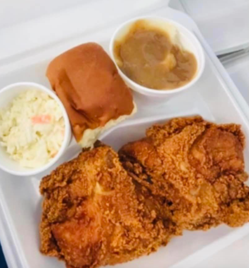 A takeout tray with two pieces of fried chicken, coleslaw, a roll, and a serving of gravy.