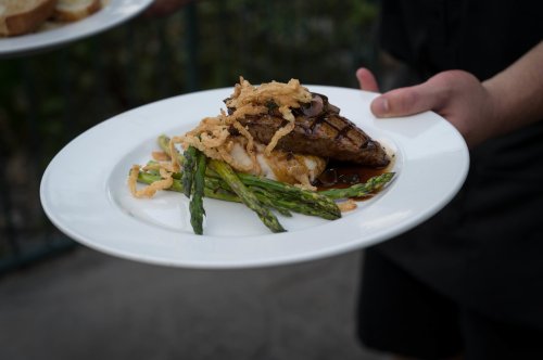 A plate of grilled meat topped with crispy onions, served with asparagus and a side of mashed potatoes.