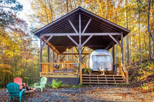 A cozy trading post with an Airstream trailer, surrounded by autumn trees and colorful outdoor seating.