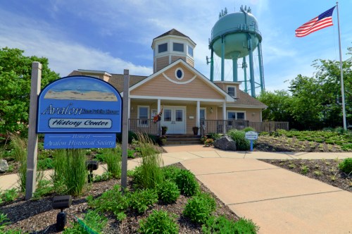 A charming history center with a water tower in the background, surrounded by greenery and a clear blue sky.
