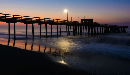 A serene pier at sunset, with soft waves lapping at the shore and a glowing light illuminating the scene.