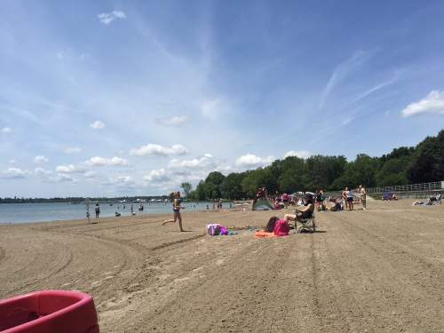 A sandy beach with people enjoying the sun, playing, and relaxing by the water under a blue sky with fluffy clouds.