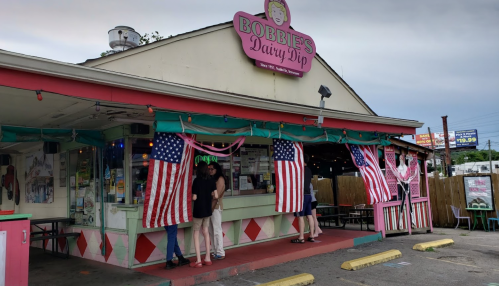 Exterior of Bobbie's Dairy Dip, featuring American flags and colorful decor, with people standing outside.