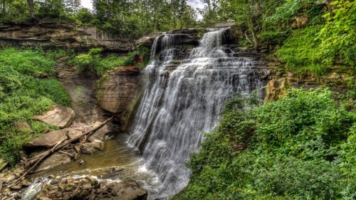 A serene waterfall cascading over rocky cliffs, surrounded by lush green foliage and a tranquil stream below.