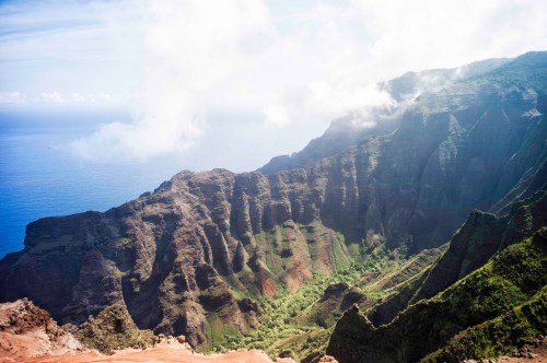A breathtaking view of rugged cliffs and lush greenery overlooking the ocean, with clouds drifting above.