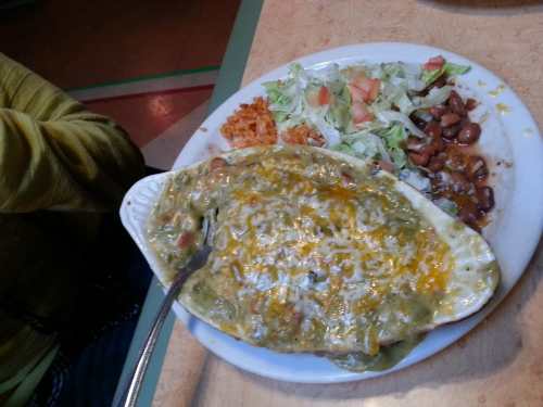 A plate of enchiladas topped with green sauce and cheese, served with rice, beans, and a side salad.
