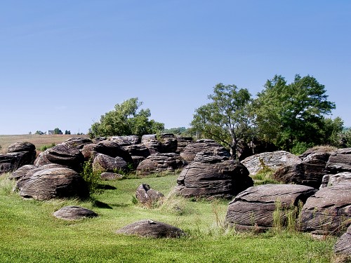 A landscape featuring large, weathered rocks scattered across green grass under a clear blue sky.