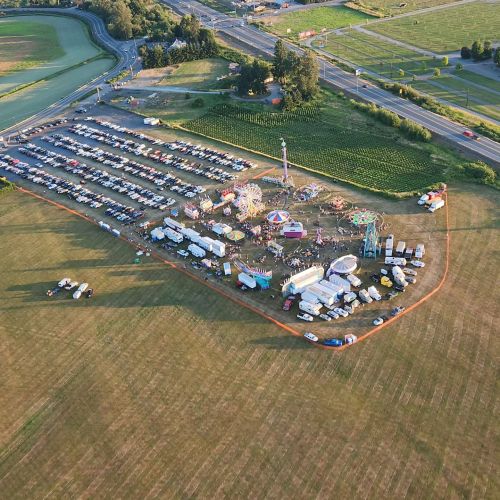 Aerial view of a fairground with rides, food stalls, and a large parking area filled with cars.