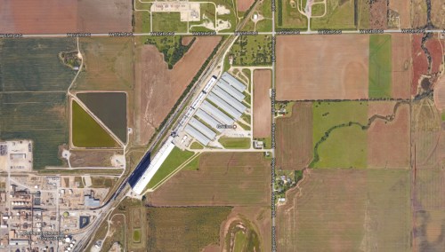 Aerial view of agricultural land with fields, a large building, and roads intersecting in a rural area.