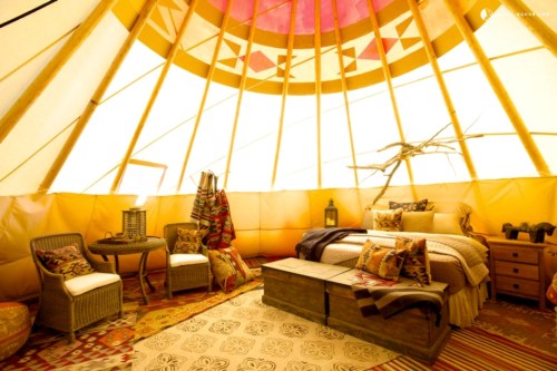 Cozy interior of a tent with a bed, seating area, and decorative patterns, illuminated by warm, natural light.