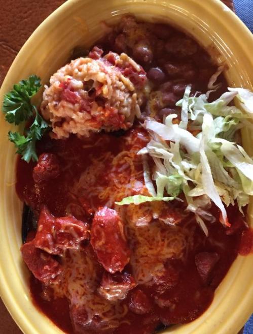 A colorful plate featuring rice, beans, lettuce, and a meat dish topped with red sauce and cheese.