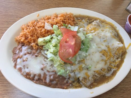 A plate of enchiladas topped with cheese, served with refried beans, rice, lettuce, and tomato.