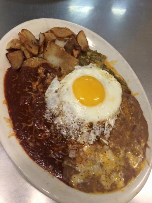 A plate of huevos rancheros with a fried egg, cheese, green sauce, and crispy potatoes on the side.