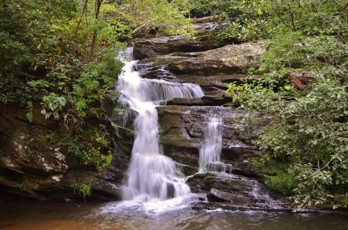 A serene waterfall cascading over moss-covered rocks, surrounded by lush green foliage.