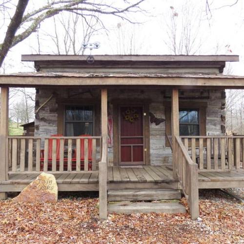 A rustic wooden cabin with a porch, red chairs, and a welcoming front door surrounded by bare trees.