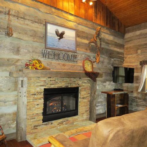 Cozy interior with wooden walls, a fireplace, a welcome sign, and rustic decor, creating a warm atmosphere.