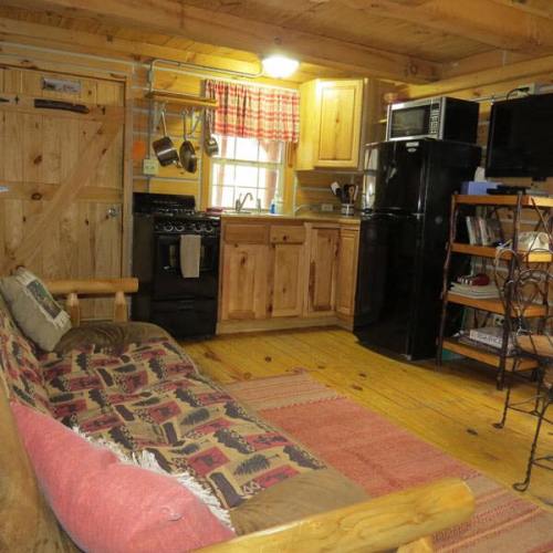 Cozy wooden cabin interior with a kitchen, sofa, and rustic decor, featuring warm lighting and a welcoming atmosphere.