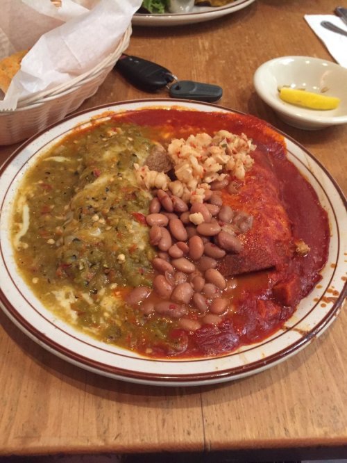 A plate of enchiladas topped with red and green sauces, accompanied by rice and pinto beans.