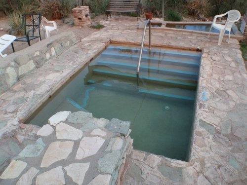 A stone-lined pool with steps, surrounded by a patio and chairs, set in a natural outdoor environment.