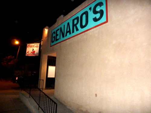 Exterior of a building at night with a sign reading "Genaro's" and a Coca-Cola advertisement visible.