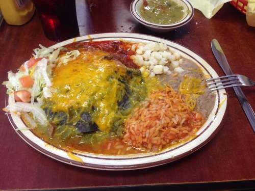 A plate of enchiladas topped with cheese, served with rice, beans, salad, and salsa on a wooden table.