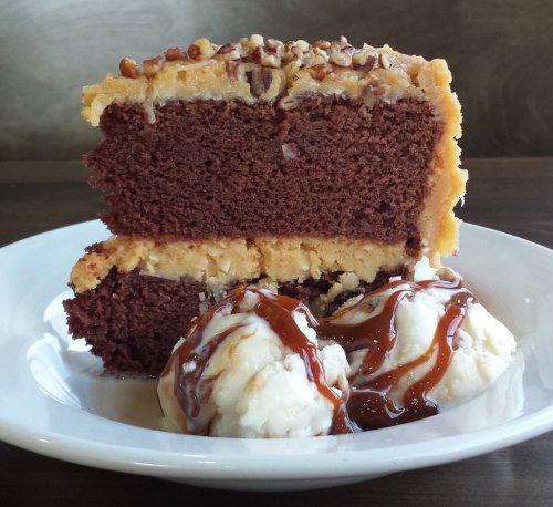 A slice of chocolate cake with a creamy frosting, served with two scoops of vanilla ice cream drizzled with caramel.