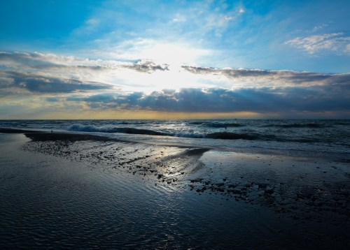 A serene beach scene at sunset, with gentle waves and a cloudy sky reflecting warm hues.