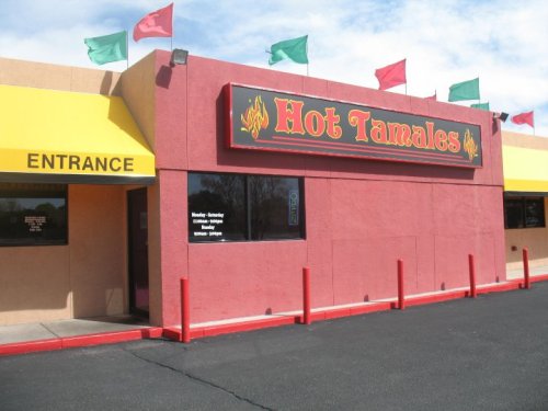 Exterior of a restaurant named "Hot Tamales," featuring colorful flags and a yellow entrance awning.