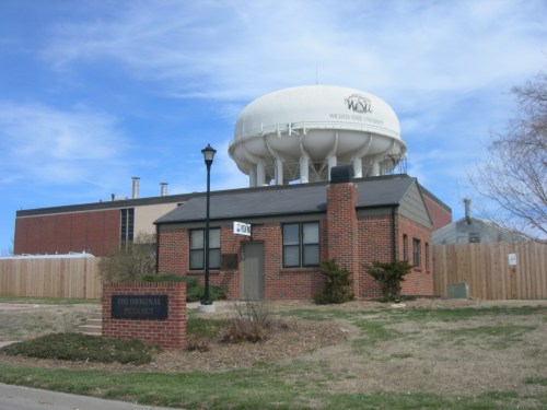 A brick building with a sign, next to a large water tower, under a blue sky with scattered clouds.